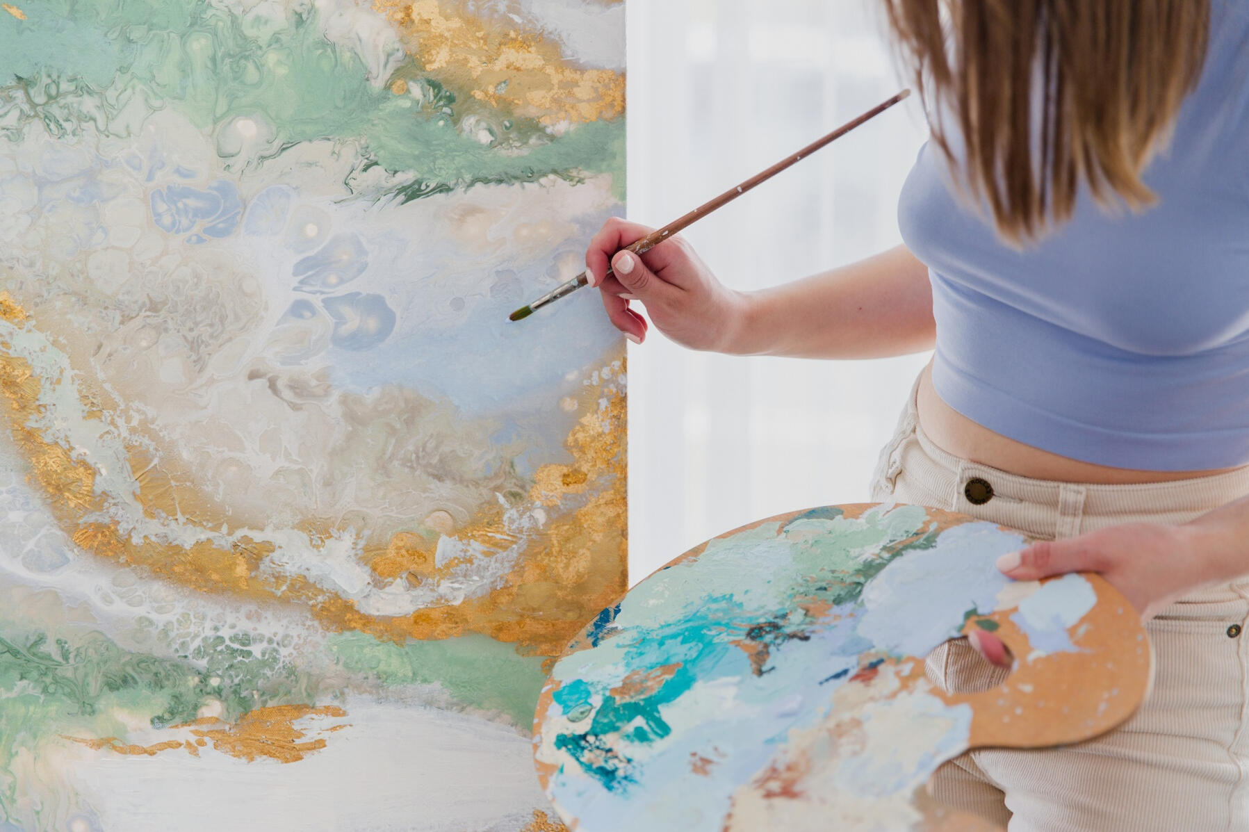 Custom painting by abstract artist Kayley Woods Kayley holds a paintbrush and paint palette to a large green and gold abstract artwork